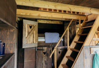 Intérieur d'une cabane rustique avec mezzanine, escalier et lit à la Wood Lodge, Duynpark Het Zwanenwater, Pays-Bas.