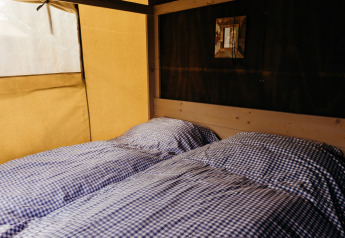 Deux lits simples avec des draps à carreaux bleus et blancs dans une tente safari au Wood Lodge, Duynpark Het Zwanenwater.