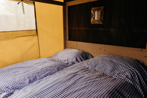 Dos camas individuales con sábanas de cuadros azules y blancas en una tienda safari de Wood Lodge, Duynpark Het Zwanenwater.
