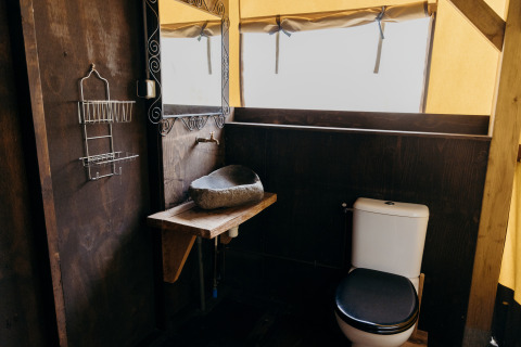 Baño en tienda safari Wood Lodge, Duynpark Het Zwanenwater, Países Bajos, con inodoro y lavabo de piedra.