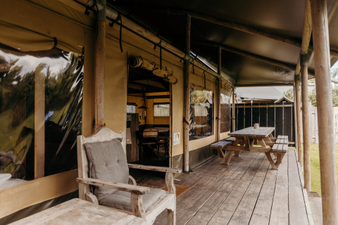 Wooden terrace with benches and chairs outside a safari tent named Wood Lodge at Duynpark Het Zwanenwater, Netherlands.