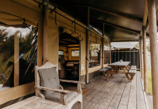 Terraza de madera con bancos y sillas junto a una tienda safari llamada Wood Lodge en Duynpark Het Zwanenwater, Países Bajos.