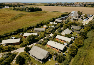 Vista aérea de una zona de tiendas safari rodeada de vegetación y campos bajo un cielo azul claro.