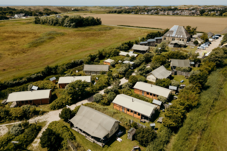 Luchtfoto van een safaritentenpark omgeven door groen en velden onder een heldere blauwe lucht.