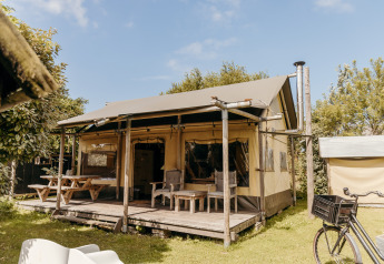 Tienda safari Beach Lodge con porche, asientos al aire libre, mesas de picnic y bicicleta en entorno verde.