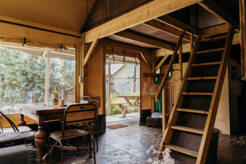 Interior de la tienda safari Beach Lodge en Duynpark Het Zwanenwater, con mesa de comedor y escalera al altillo.