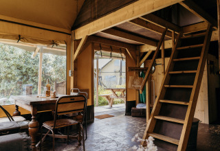 Interior de la tienda safari Beach Lodge en Duynpark Het Zwanenwater, con mesa de comedor y escalera al altillo.