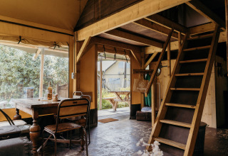 Interior of the Beach Lodge safari tent at Duynpark Het Zwanenwater, featuring dining table and loft stairs.