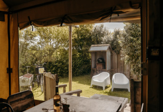 Vista desde una tienda safari hacia un jardín con sillas blancas, barbacoa y bicicletas en Duynpark Het Zwanenwater.