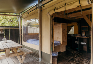 Interior y exterior de tienda safari Beach Lodge en Duynpark Het Zwanenwater, Países Bajos, con muebles de madera.