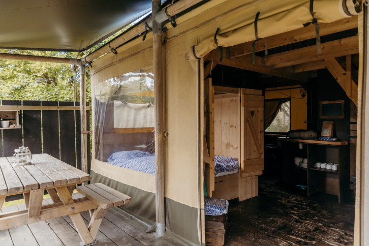 Interieur en terras van safaritent Beach Lodge bij Duynpark Het Zwanenwater in Nederland met houten meubels.