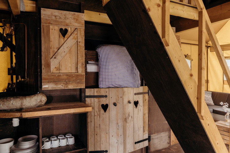 Interieur van Beach Lodge safaritent bij Duynpark Het Zwanenwater, Nederland, met houten meubels en bed.