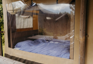 Interior de una tienda safari Beach Lodge en Duynpark Het Zwanenwater, Países Bajos, con cama y ropa de cuadros.