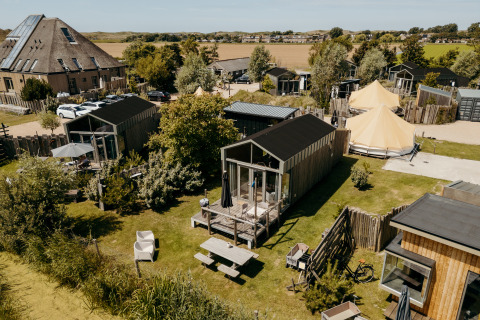 Vista aérea de Rescue cottage, una tiny house con terraza, jardín y pequeñas casas alrededor en el campo.