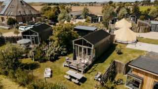 Vista aérea de Rescue cottage, una tiny house con terraza, jardín y pequeñas casas alrededor en el campo.