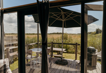 View from Rescue cottage at Duynpark Het Zwanenwater, Netherlands, showing deck, table, and umbrella.