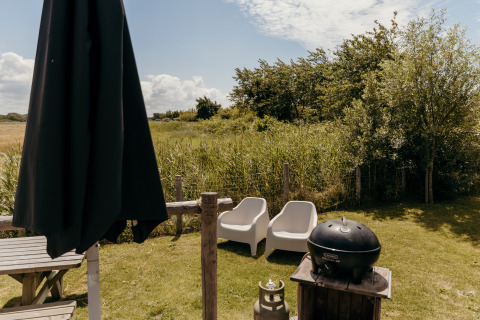 Outdoor area at Rescue cottage in Duynpark Het Zwanenwater, Netherlands, featuring chairs, umbrella and grill.
