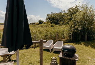 Outdoor area at Rescue cottage in Duynpark Het Zwanenwater, Netherlands, featuring chairs, umbrella and grill.