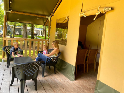 Familie sidder og slapper af på træterrassen i et glampingtelt ved Vakantiepark Bonte Vlucht, Utrecht.