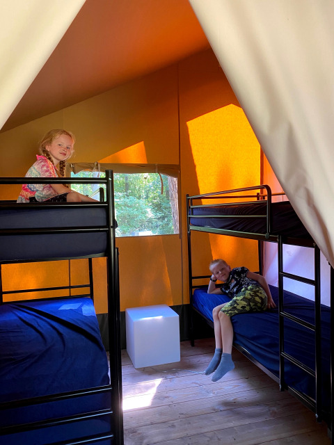 Twee kinderen ontspannen op stapelbedden in een tent met oranje wanden bij Vakantiepark Bonte Vlucht, Utrecht.