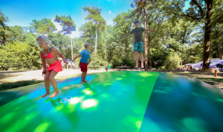 Børn leger og hopper på en stor oppustelig pude i en skovklædt feriepark i Utrecht, Holland.