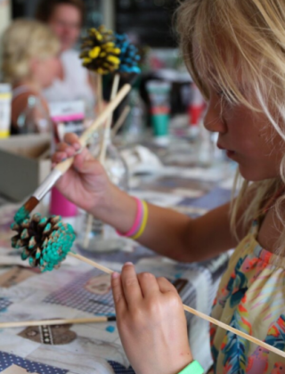 Et barn maler en grankogle med farver som en del af en kreativ aktivitet på Vakantiepark Bonte Vlucht.