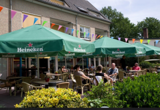 Terraza al aire libre en Vakantiepark Bonte Vlucht, Utrecht, Países Bajos, con sombrillas verdes de Heineken.
