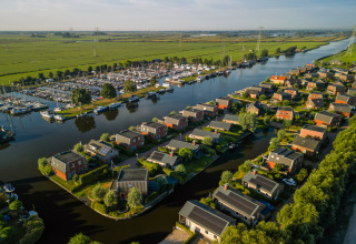 Vue aérienne d’un hébergement glamping près d’une rivière, entouré de champs verts et d’un port de plaisance.