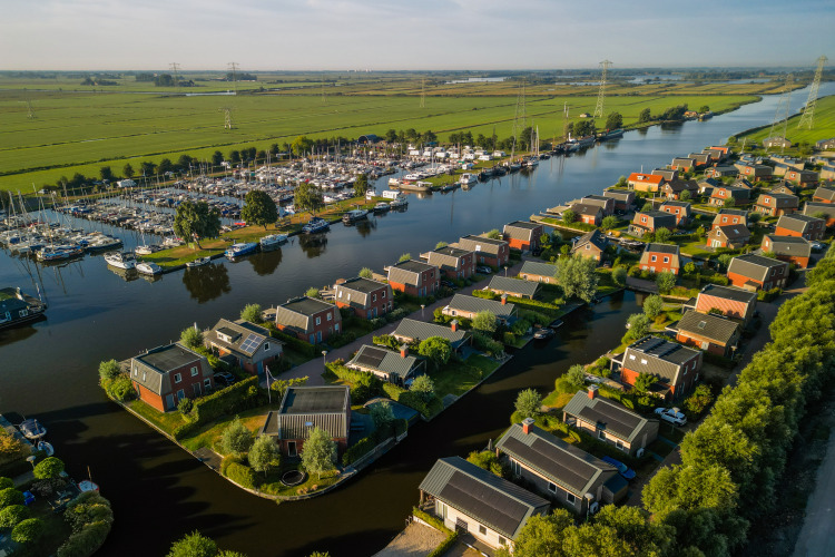 Aerial view of glamping accommodation by a river, surrounded by green fields and a marina with boats.