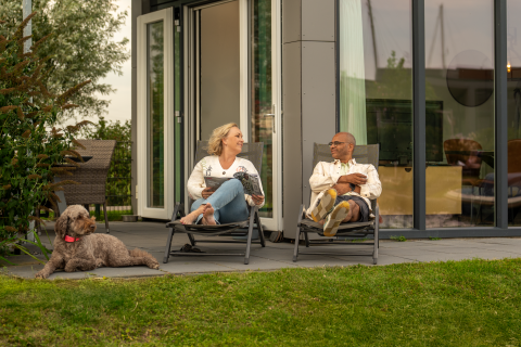 Ein Paar entspannt sich mit einem Hund vor ihrem Tiny House Knilles bei Tusken de Marren in den Niederlanden.