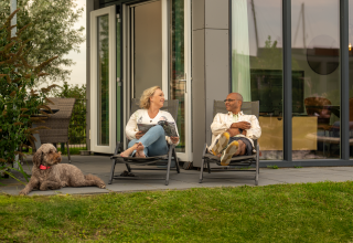 Ein Paar entspannt sich mit einem Hund vor ihrem Tiny House Knilles bei Tusken de Marren in den Niederlanden.