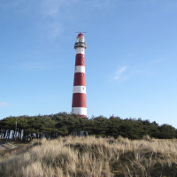 Faro de franjas rojas y blancas cerca de Hollum, Frisia, Países Bajos, rodeado de dunas y pinos bajo un cielo azul claro.