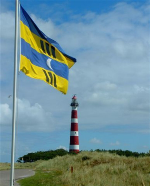 La bandiera di Ameland sventola al vento al Parc Koudenburg, con l’iconico faro rosso e bianco sullo sfondo.