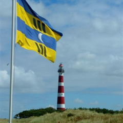 La bandera de Ameland ondea al viento en Parc Koudenburg, con el icónico faro rojo y blanco de fondo.