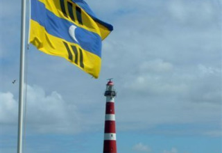 Le drapeau d'Ameland flotte au vent à Parc Koudenburg, avec le phare rouge et blanc emblématique en arrière-plan.