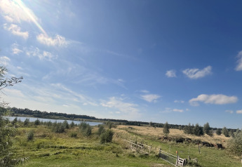 Udsigt fra en lille hytte ved Holiday park Eigen Wijze i Holland med grønne marker og en blå himmel.