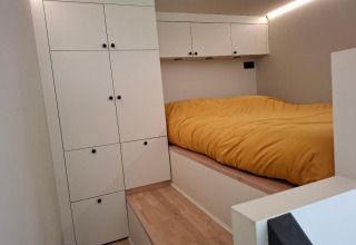 Moderne compacte slaapkamer met witte kasten en geel beddengoed in tiny house bij Holiday park Eigen Wijze.