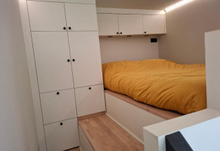 Moderne lille soveplads med opbevaringsskabe og gul sengelinned i Tiny house i Holiday park Eigen Wijze.