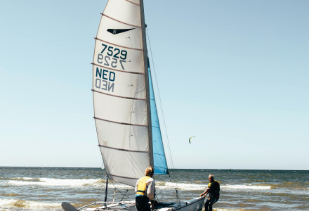 Dos personas empujan un catamarán hacia el mar cerca de Hollum, Frisia, Países Bajos, en un día soleado.