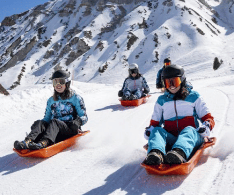 Quatre personnes font de la luge sur une pente enneigée entourée de montagnes près de Champagny-en-Vanoise, France.
