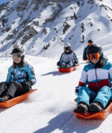 Quatre personnes font de la luge sur une pente enneigée entourée de montagnes près de Champagny-en-Vanoise, France.