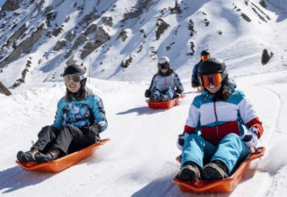 Four people sledding down a snowy slope surrounded by mountains near Champagny-en-Vanoise, France.