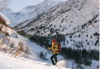 A hiker in yellow jacket and red beanie climbs a snowy slope in the Alps at Les Chalets Huttopia Champagny.