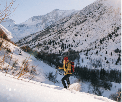 A hiker in yellow jacket and red beanie climbs a snowy slope in the Alps at Les Chalets Huttopia Champagny.