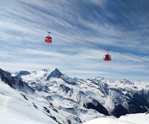 Two red cable cars travel above snowy Alpine mountains at Champagny en Vanoise, Auvergne-Rhône-Alpes, France.