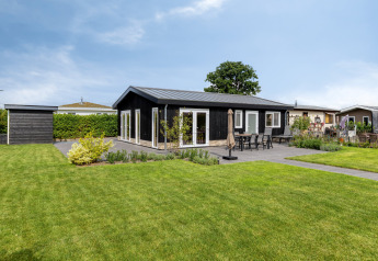 Moderne lodge ved navn Natuurhoeve med sort facade, stor terrasse og grøn have under blå himmel.