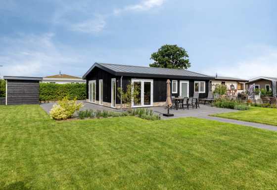 Moderne Lodge namens Natuurhoeve mit schwarzer Fassade, Terrasse und gepflegtem Rasen im Freien.