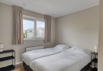 Chambre avec deux lits simples, draps blancs, tables de chevet et fenêtre dans un lodge à Natuurhoeve, Park Westerkogge, Pays-Bas.