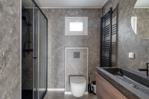 Salle de bains moderne avec murs en marbre, douche vitrée, WC suspendu et lavabo noir à Natuurhoeve, Park Westerkogge.
