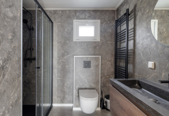 Salle de bains moderne avec murs en marbre, douche vitrée, WC suspendu et lavabo noir à Natuurhoeve, Park Westerkogge.
